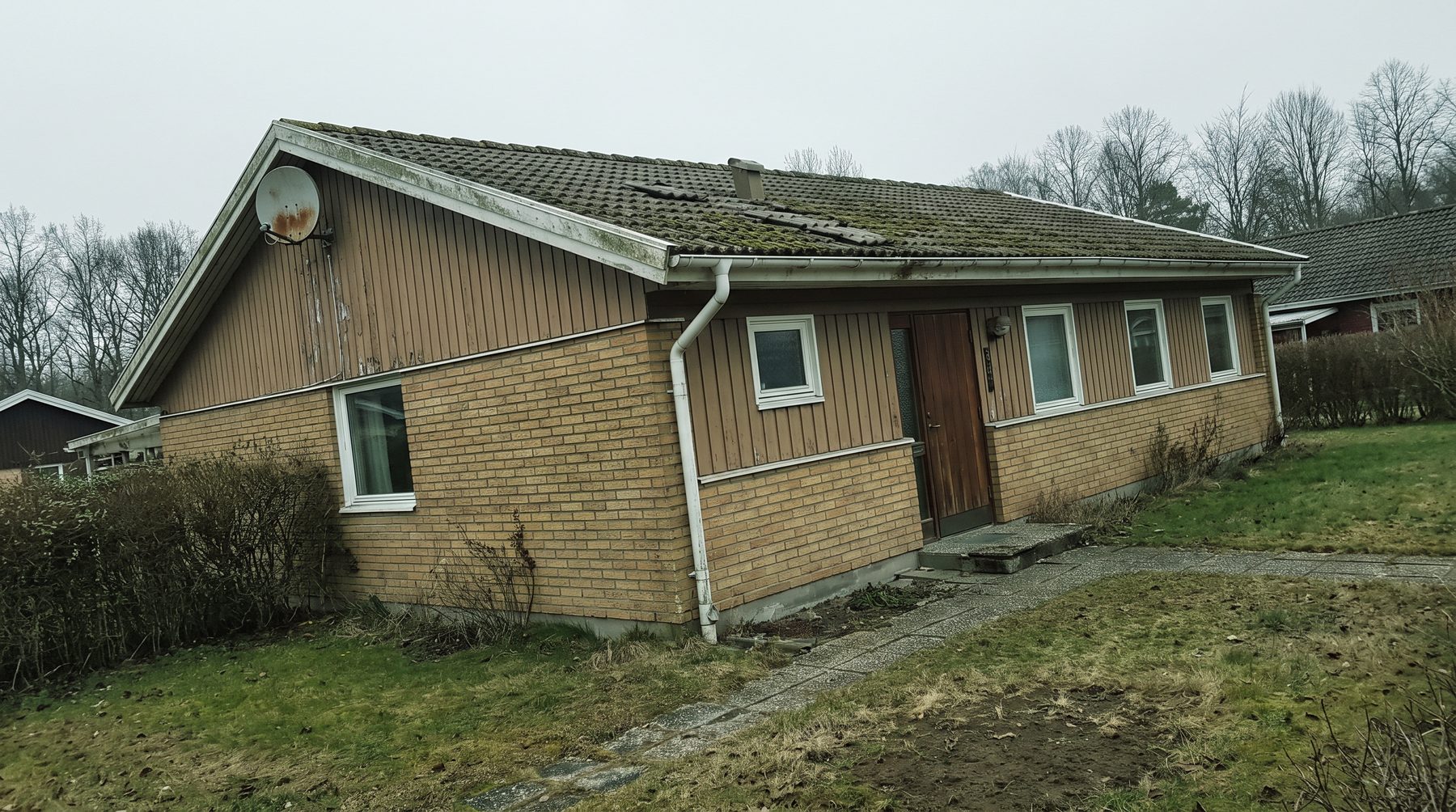 Gul tegelvilla med mossigt betongtegeltak, fotograferad en mulen dag.
