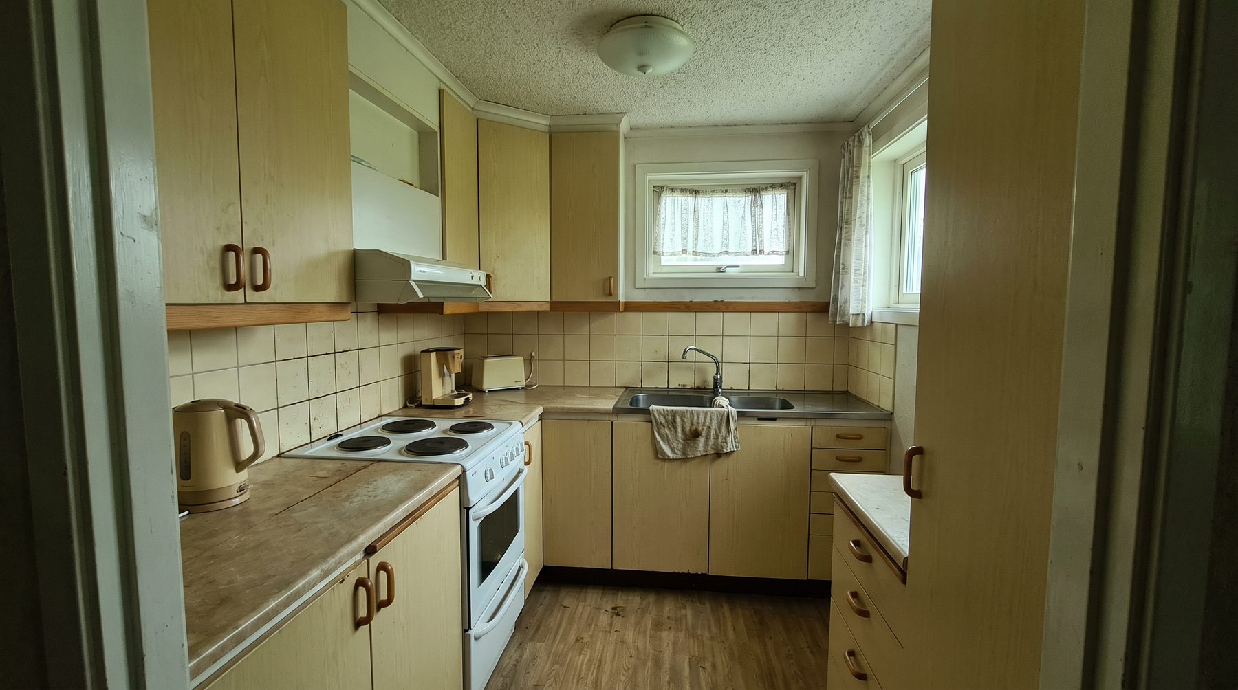 Gulnat kök med laminatluckor, kaklat stänkskydd och vinylgolv.