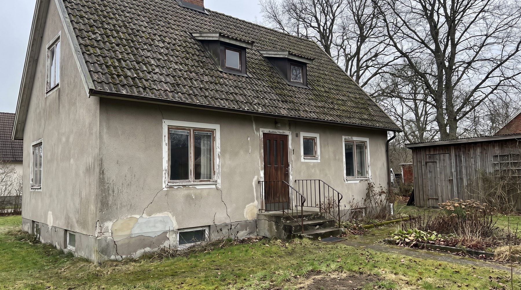 Villa med sprucken puts, gammalt tak och ett skjul på tomten.